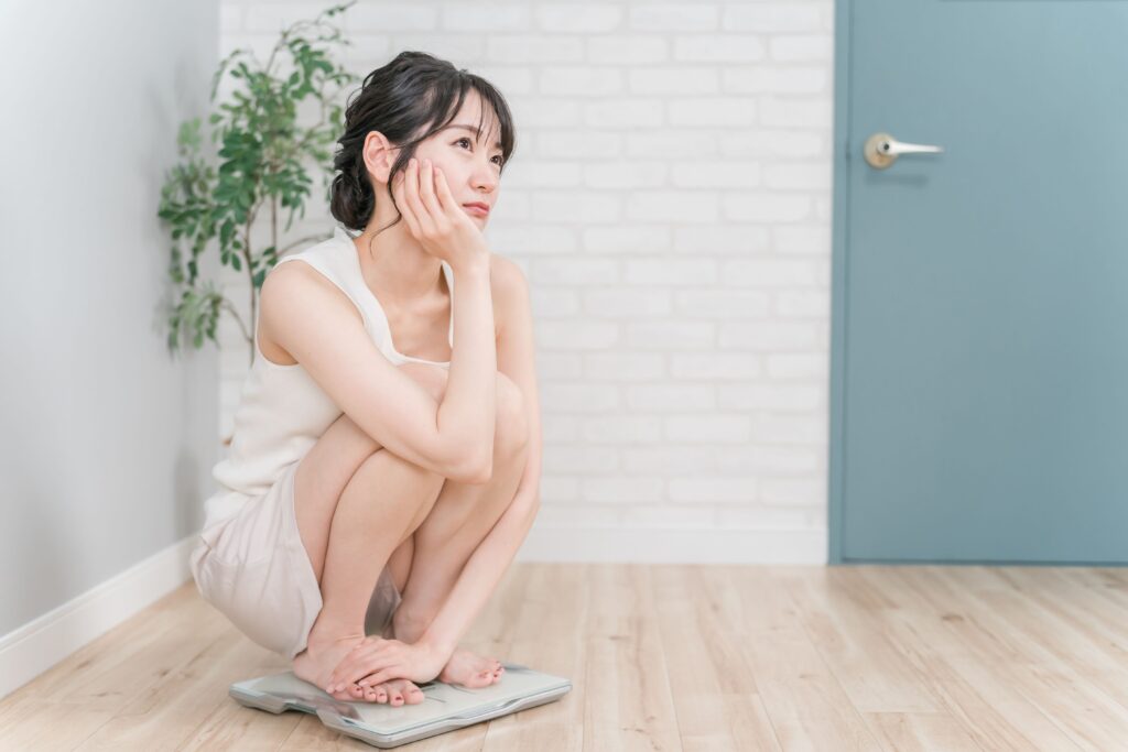 体重計の上で考える女性の写真